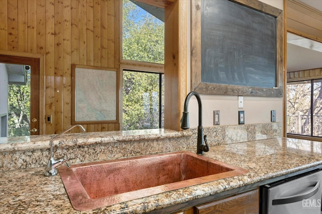 kitchen with light stone counters, sink, dishwasher, and wood walls