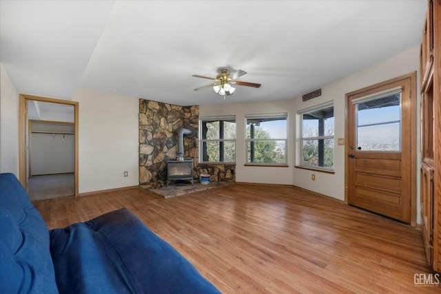 unfurnished living room featuring wood-type flooring, ceiling fan, and a wood stove