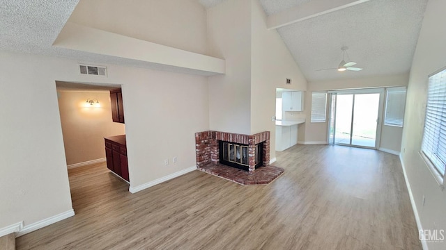 unfurnished living room featuring visible vents, baseboards, light wood-style flooring, a textured ceiling, and a fireplace