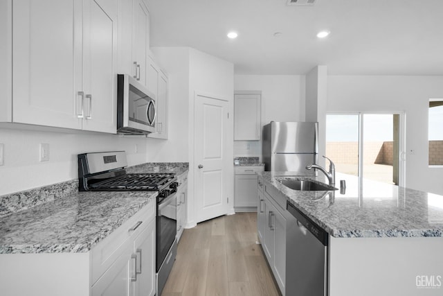 kitchen featuring light stone counters, stainless steel appliances, a kitchen island with sink, a sink, and light wood-type flooring