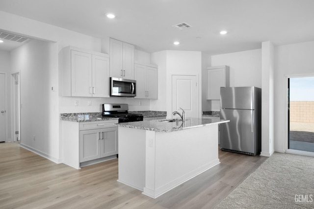 kitchen with stainless steel appliances, a center island with sink, a sink, and light stone counters