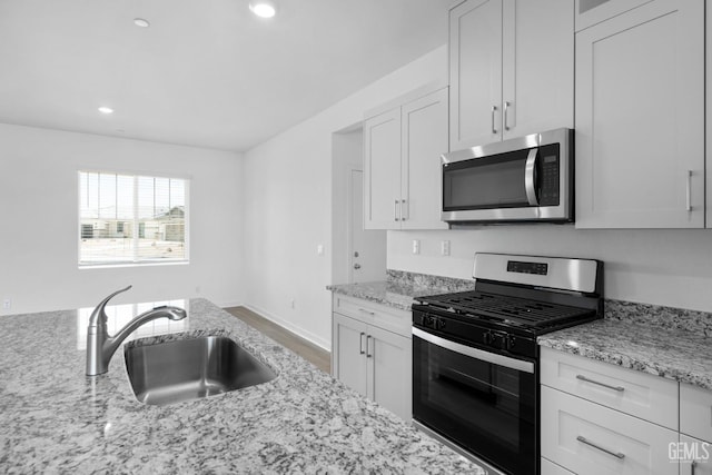 kitchen with light stone countertops, stainless steel appliances, white cabinetry, a sink, and recessed lighting