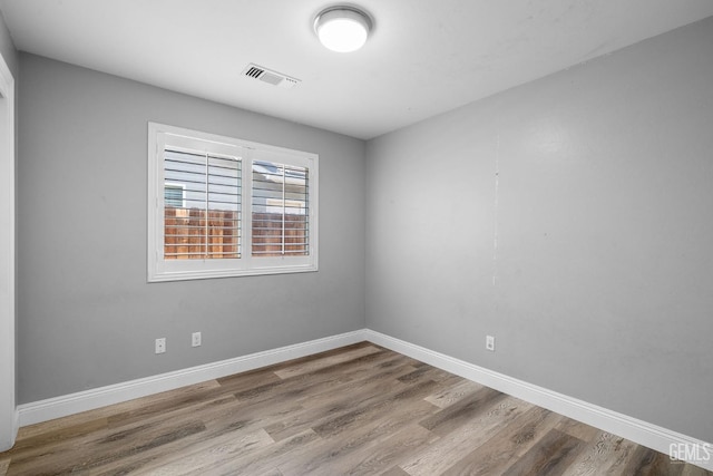 spare room featuring baseboards, visible vents, and wood finished floors