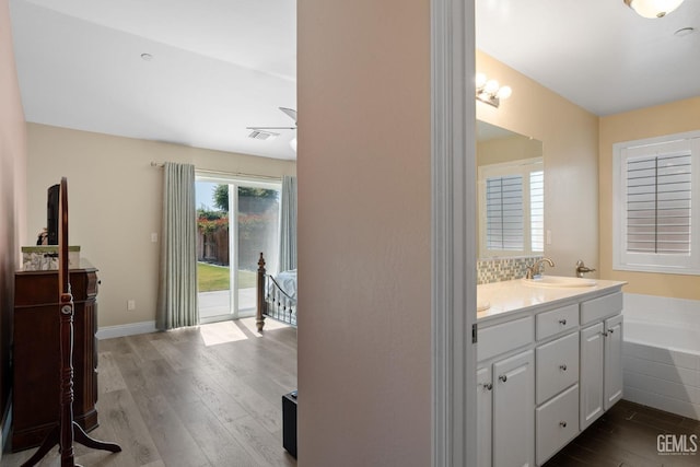 full bath featuring double vanity, a sink, wood finished floors, and a healthy amount of sunlight