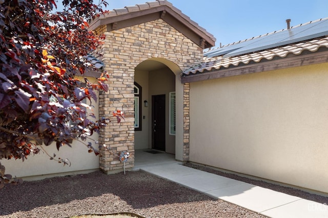 property entrance with stucco siding, stone siding, a tile roof, and solar panels