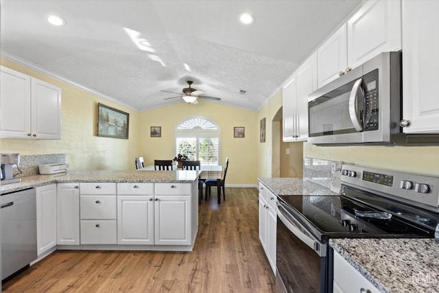 kitchen featuring stainless steel appliances, vaulted ceiling, a peninsula, a ceiling fan, and light wood-style flooring