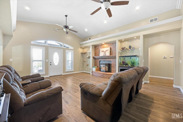 living area featuring a ceiling fan, arched walkways, wood finished floors, vaulted ceiling, and a brick fireplace