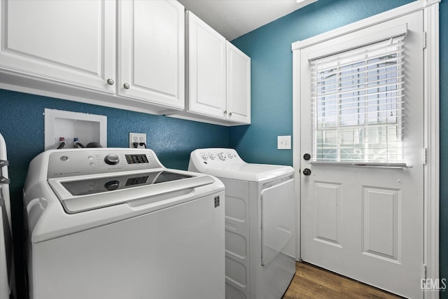 clothes washing area with washer and dryer, cabinet space, wood finished floors, and a textured wall