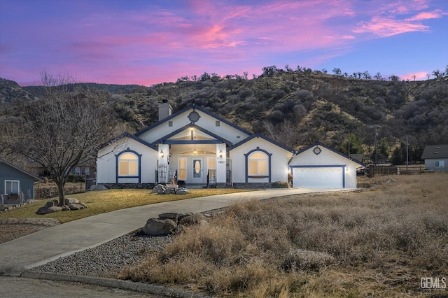 ranch-style home featuring concrete driveway, a chimney, a garage, an outbuilding, and a mountain view