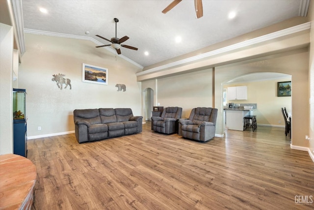 living area featuring arched walkways, ceiling fan, crown molding, wood finished floors, and vaulted ceiling