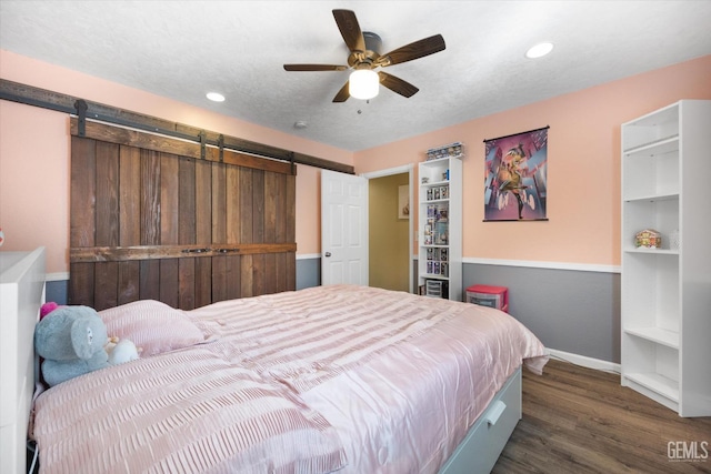 bedroom featuring baseboards, a barn door, wood finished floors, recessed lighting, and ceiling fan