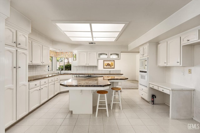 7310 Clifftop Way, Bakersfield, CA 93306 - kitchen with white appliances, a breakfast bar area, white cabinets, and decorative backsplash