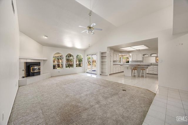 7310 Clifftop Way, Bakersfield, CA 93306 - unfurnished living room featuring light tile patterned floors, a ceiling fan, high vaulted ceiling, a tiled fireplace, and light carpet