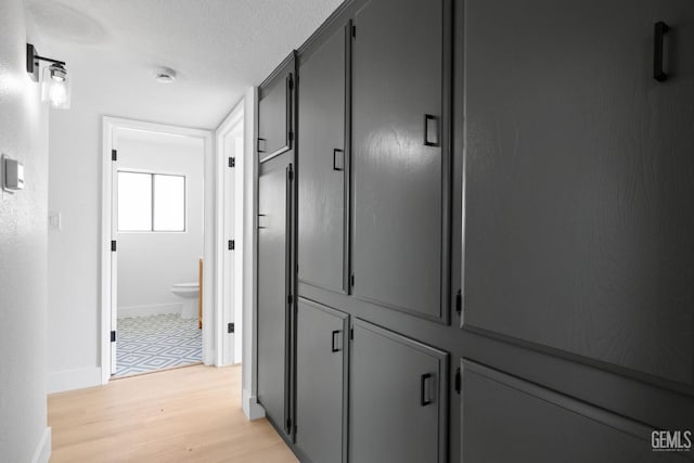 hall with a textured ceiling, light wood finished floors, and baseboards