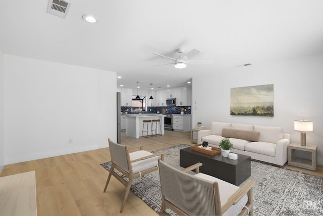 living room featuring light wood finished floors, visible vents, and a ceiling fan