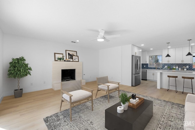 living area featuring a fireplace with raised hearth, recessed lighting, a ceiling fan, visible vents, and light wood-style floors