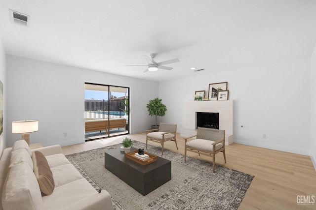 living room with a brick fireplace, wood finished floors, visible vents, and baseboards