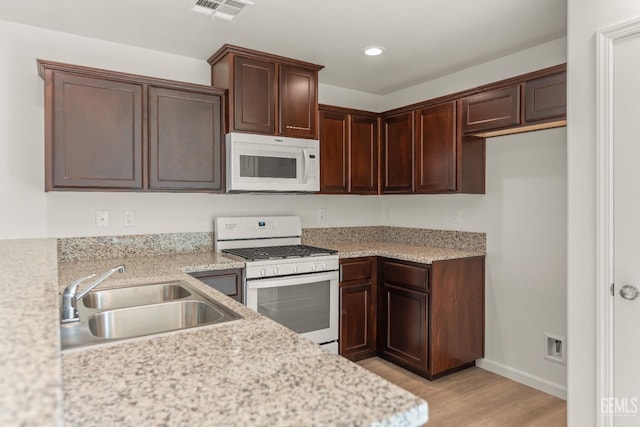 kitchen featuring light stone counters, sink, white appliances, and light wood-type flooring