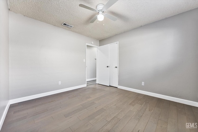 unfurnished room with visible vents, ceiling fan, a textured ceiling, wood finished floors, and baseboards