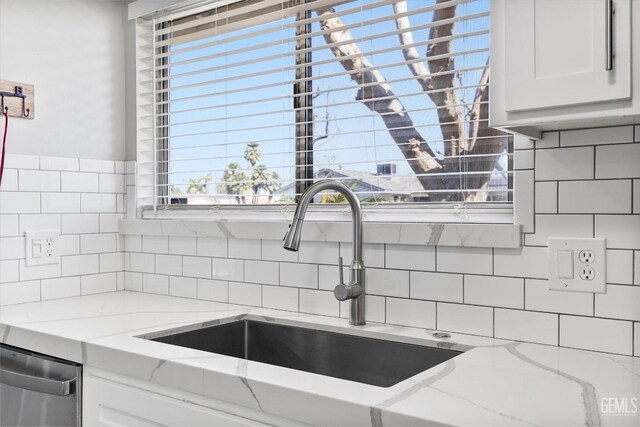 kitchen with stainless steel dishwasher, a sink, white cabinets, and light stone countertops