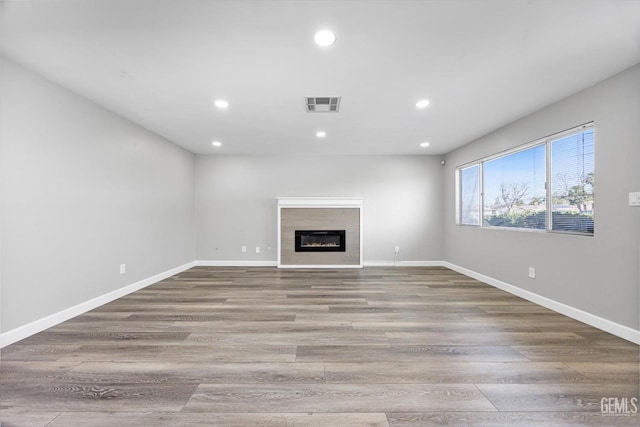 unfurnished living room featuring a glass covered fireplace, visible vents, baseboards, and wood finished floors