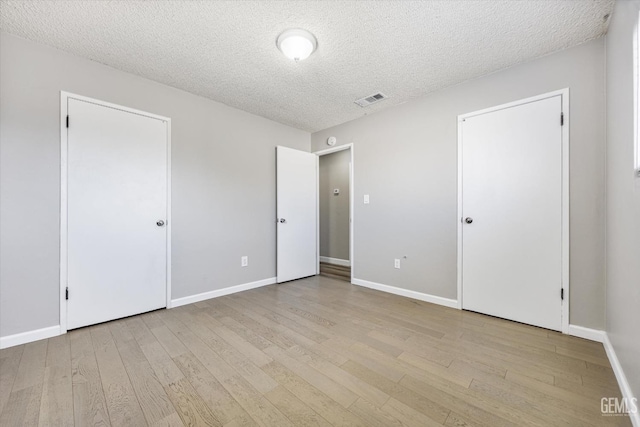 unfurnished bedroom featuring baseboards, a textured ceiling, visible vents, and light wood-style floors