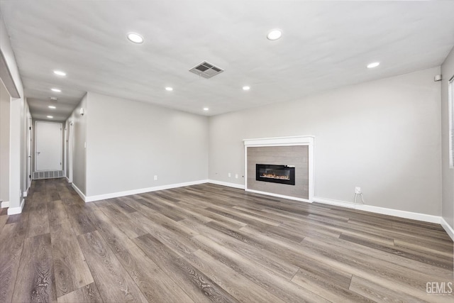 unfurnished living room with baseboards, visible vents, a tiled fireplace, wood finished floors, and recessed lighting