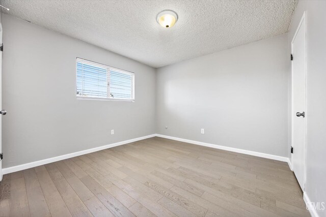 empty room with a textured ceiling, light wood-type flooring, and baseboards