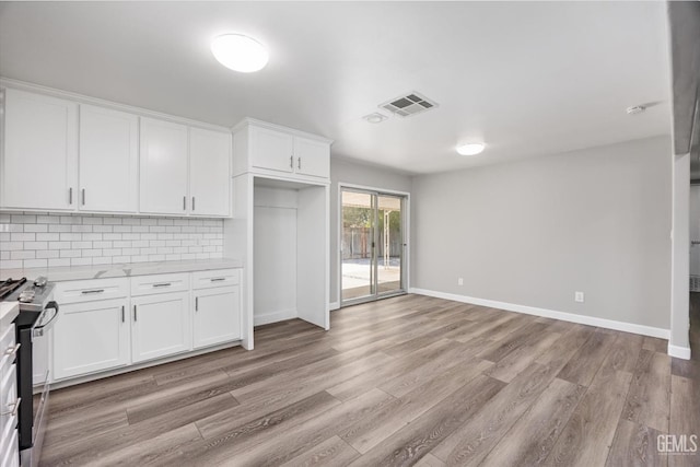 kitchen featuring tasteful backsplash, stainless steel range with gas stovetop, white cabinetry, and visible vents