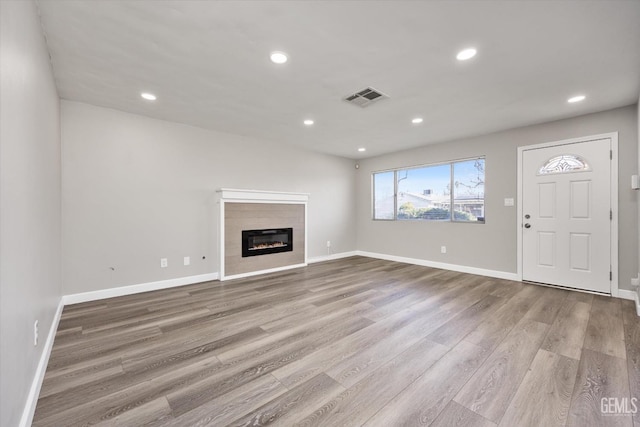 unfurnished living room featuring recessed lighting, visible vents, light wood-style flooring, a glass covered fireplace, and baseboards