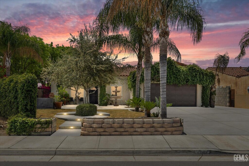 view of property hidden behind natural elements with driveway, stucco siding, and an attached garage
