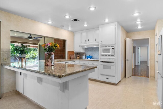 2513 Elm St, Bakersfield, CA 93301 - kitchen with white appliances, white cabinets, dark stone countertops, a breakfast bar, and under cabinet range hood