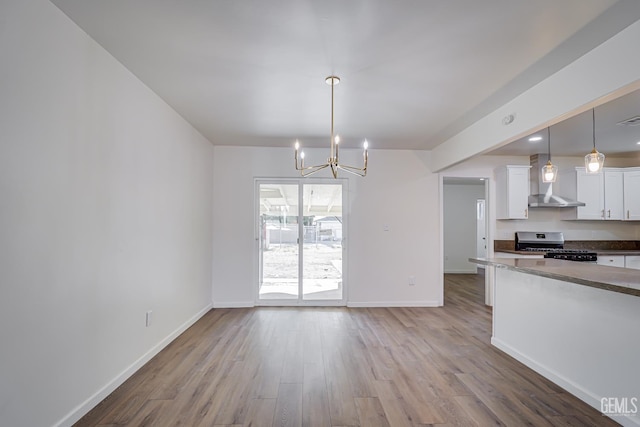 1201 Quincy St, Delano, CA 93215 - kitchen featuring stove, wall chimney range hood, a chandelier, wood finished floors, and white cabinetry