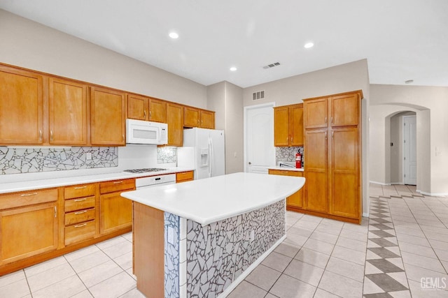 kitchen with light countertops, a center island, brown cabinetry, white appliances, and arched walkways