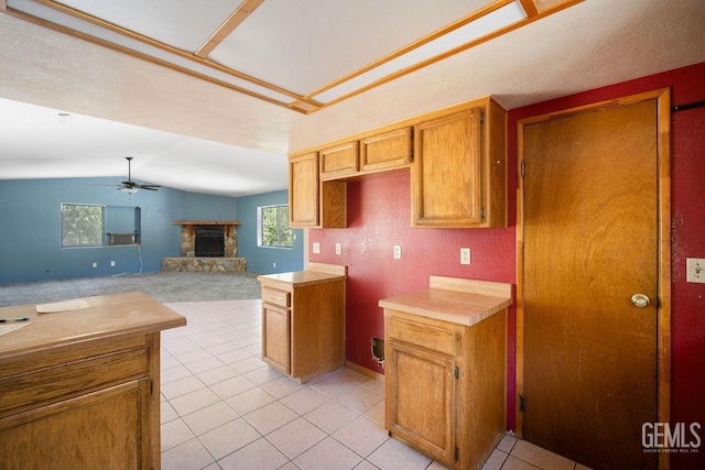 4120 Willow Trl, Frazier Park, CA 93225 - kitchen featuring a ceiling fan, a stone fireplace, light tile patterned floors, vaulted ceiling, and brown cabinets