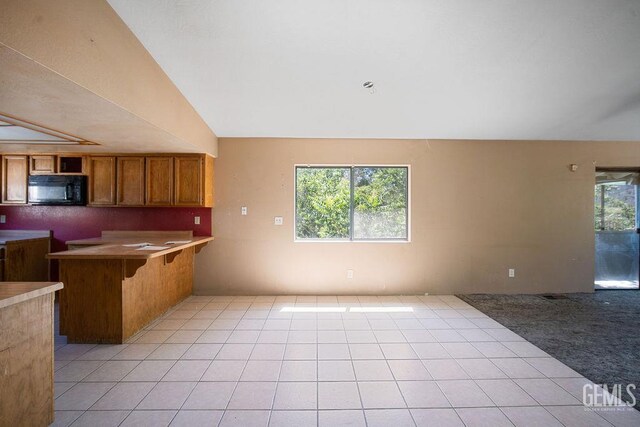 4120 Willow Trl, Frazier Park, CA 93225 - kitchen with black microwave, open floor plan, brown cabinetry, a kitchen breakfast bar, and light tile patterned floors