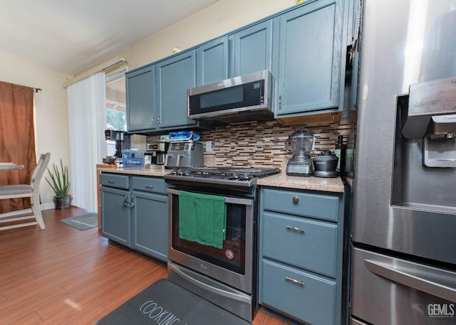 kitchen featuring hardwood / wood-style flooring, blue cabinetry, stainless steel appliances, and backsplash