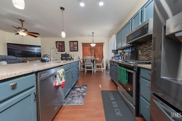 kitchen featuring pendant lighting, decorative backsplash, blue cabinetry, a textured ceiling, and stainless steel appliances