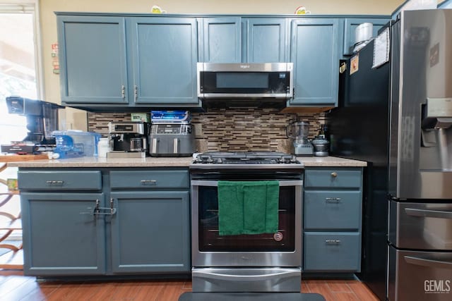 kitchen with appliances with stainless steel finishes, decorative backsplash, blue cabinets, and hardwood / wood-style floors