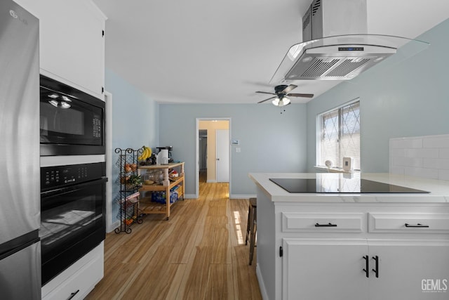 kitchen featuring light wood finished floors, island exhaust hood, light countertops, black appliances, and white cabinetry