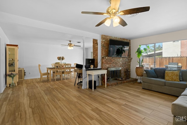 living room with light wood finished floors, a brick fireplace, a ceiling fan, and baseboards