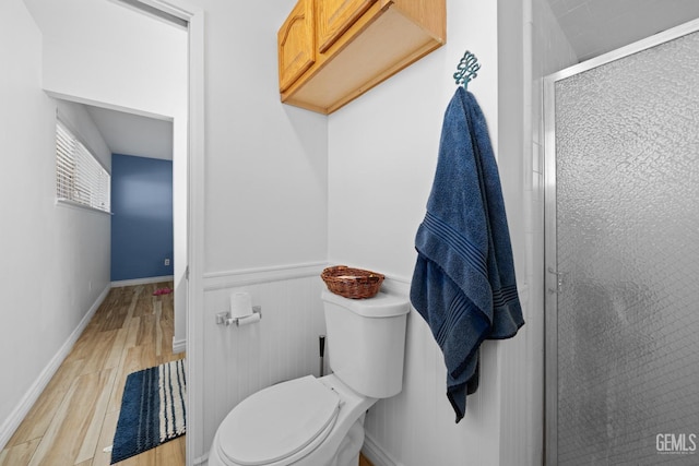 full bath with a stall shower, wainscoting, wood finished floors, and toilet