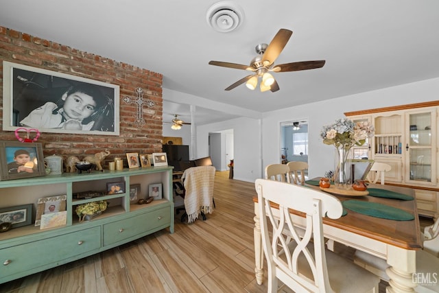 dining area with brick wall, visible vents, ceiling fan, and wood finished floors