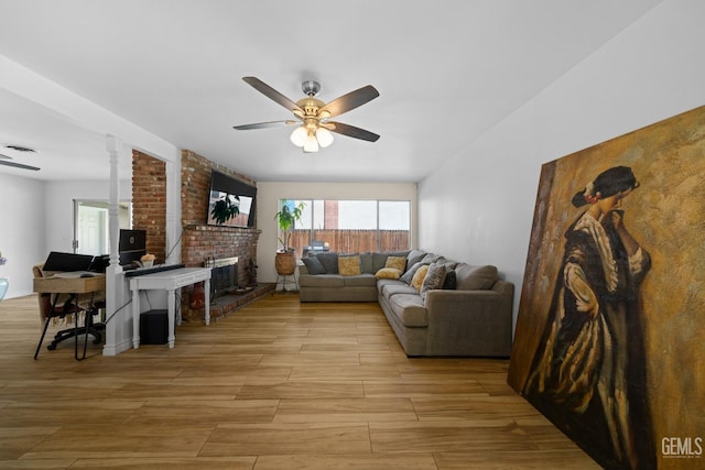 living room with a fireplace, light wood-style flooring, and a ceiling fan