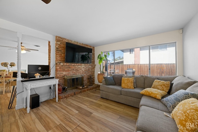 living area with a brick fireplace, ceiling fan, and light wood finished floors