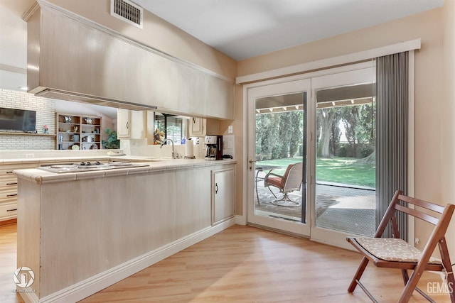 kitchen with light wood-style floors, cooktop, tile counters, and tasteful backsplash