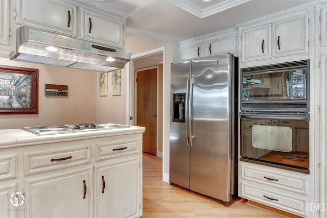 kitchen featuring crown molding, black appliances, light wood finished floors, tile counters, and under cabinet range hood