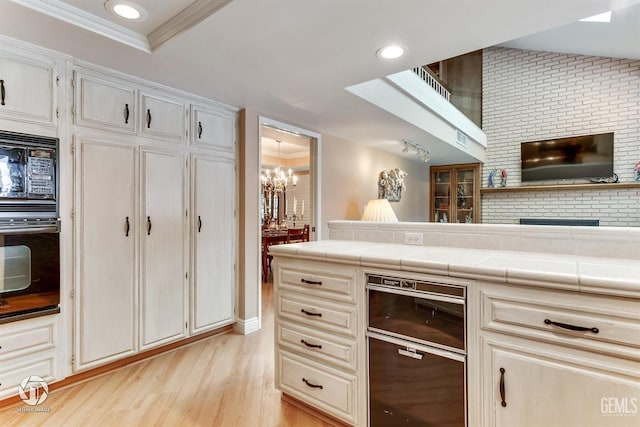 kitchen with ornamental molding, black appliances, tile countertops, light wood finished floors, and a notable chandelier