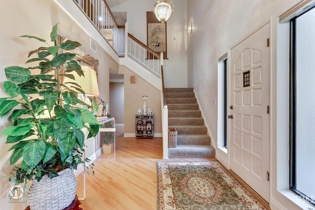 entryway featuring a high ceiling, a wealth of natural light, wood finished floors, visible vents, and stairway