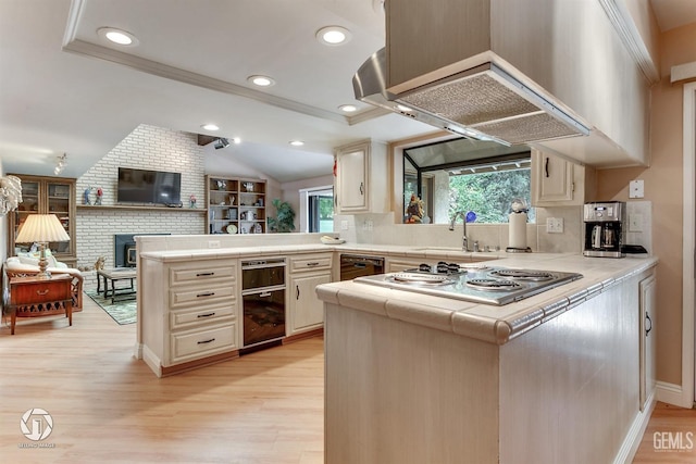kitchen with a sink, a peninsula, stainless steel electric cooktop, tile counters, and light wood-style flooring